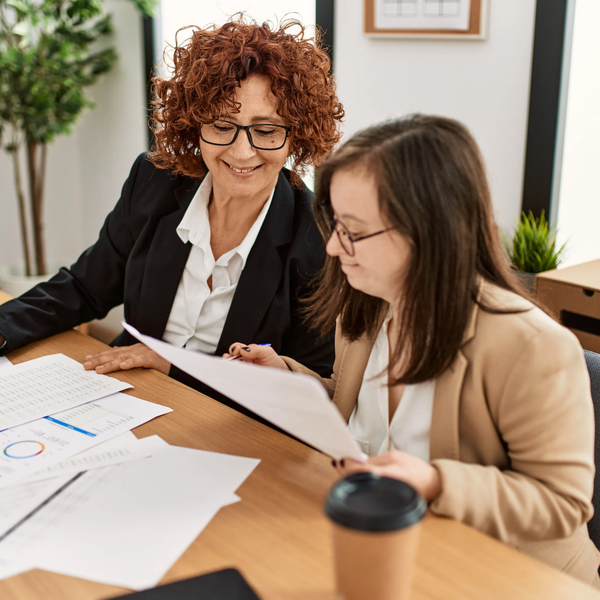 two women sitting at a desk reviewing paperwork and smiling